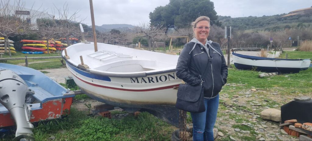 Ein Boot mit Namen Marion und Frau davor in der Cala de Portlligat