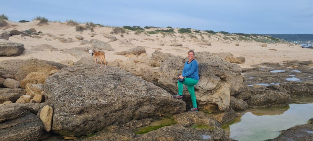 Strand mit Felsen und Frau mit Hund